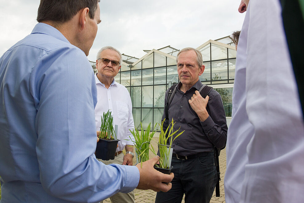 Dr. Albrecht Serfling erklärt Ehrengästen seine Arbeit. In der Hand hält er Pflanztöpfe mit kranken Weizenpflanzen.