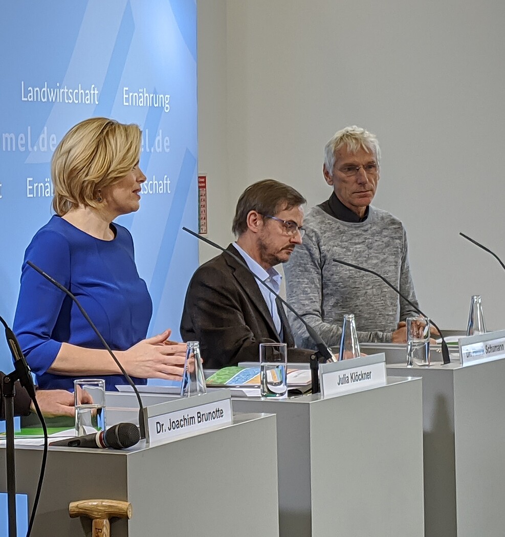 Ministerin Klöckner, Prof. Greef sowie weiterer Mann stehen an Rednerpulten