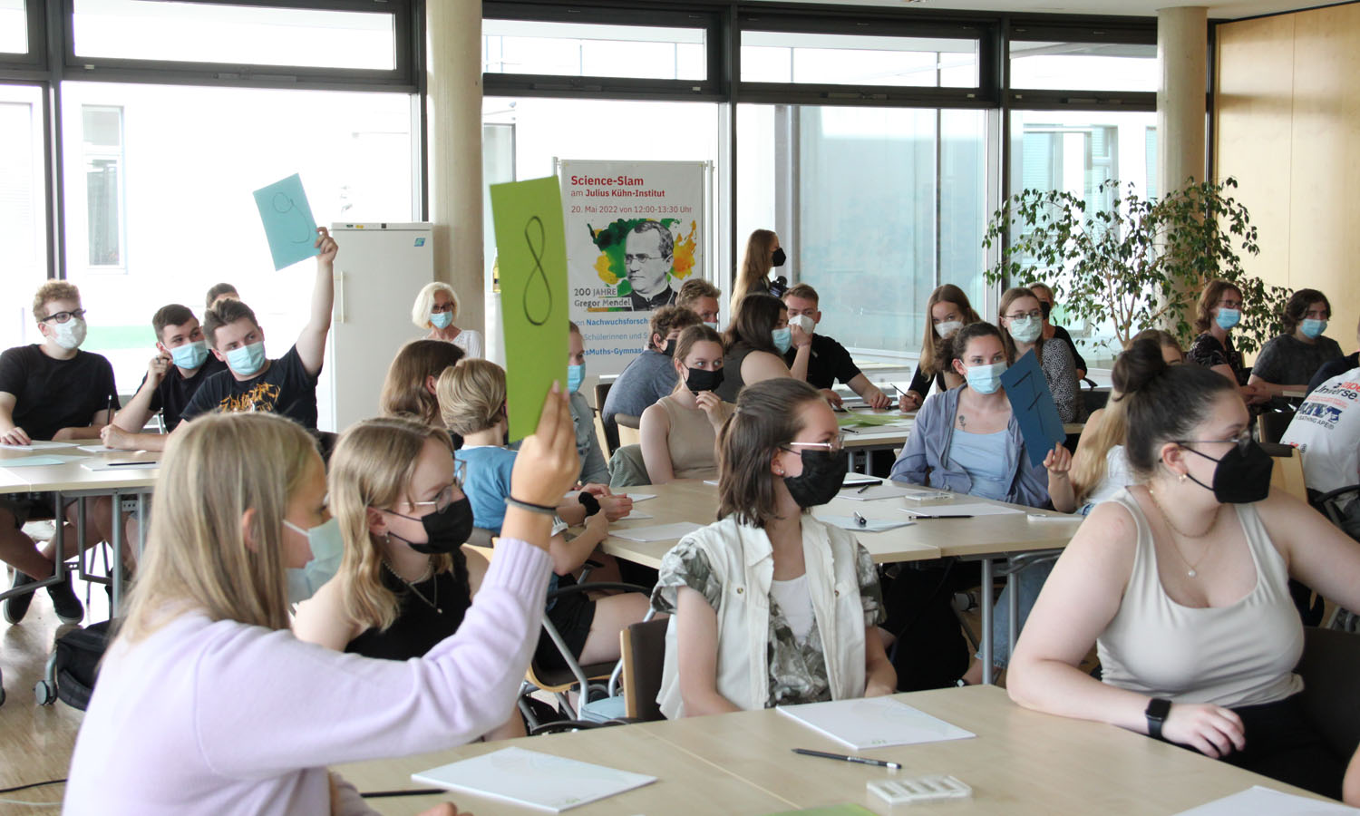 Schülerinnen und Schüler halten Punktetafeln zur Bewertung eines Science-Slam-Vortrags in die Höhe.