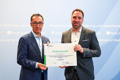 (© BMEL) Bundeslandwirtschaftsminister Cem Özdemir (links) überreicht am 19.9.2024 Dr. Til Feike vom Julius Kühn-Institut den Förderbescheid zum Verbundprojekt MagicKlimaback.