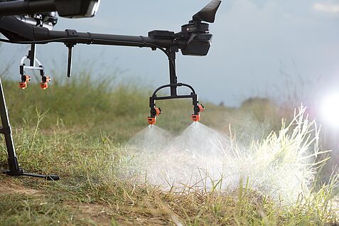 Nahaufnahme einer Drohne mit Pflanzenschutzdüsen. Ausschnitt zeigt nahzu ausschließlich die Düsen. Aus den Düsen sprüht Flüssigkeit.