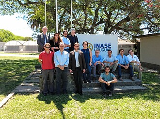 Visitors are standing or sitting on steps in front of the INASE company sign.