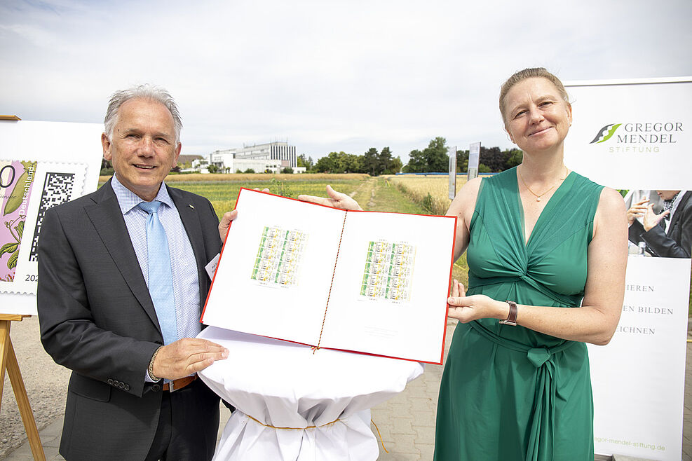 JKI-Präsident Ordon nimmt stellvertretend für das Bundesforschungsinstitut ein rotes Album mit dem Sonderpostwertzeichen "Mendel200" von der Staatssekretärin im Bundesfinanzministerium Dr. Luise Hölscher entgegen © J. Zappner/Gregor Mendel Stiftung