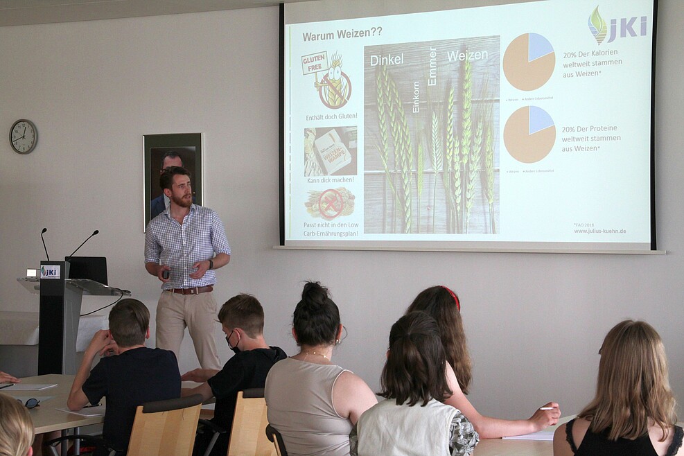 Lars Böge steht bei seinem Slam-Vortrag vor einer Folie mit Fakten über die Bedeutung von Weizen für die Ernährung der Menschheit.