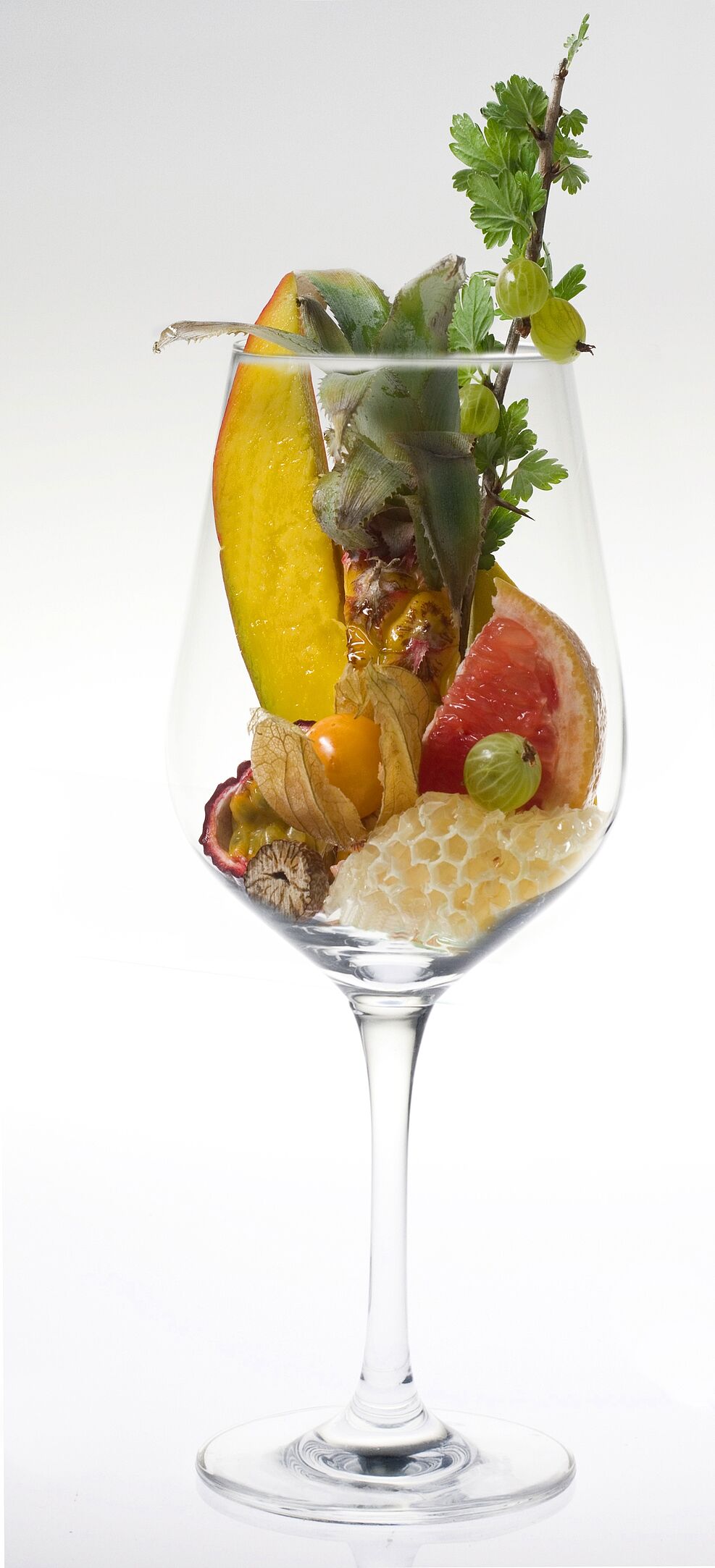 Stückchen von Ananas, Mango, Maracuja, Physalis und Stachelbeere in einem Weinglas symbolisieren das Aromaprofil der Rebsorte Calardis Musqué.