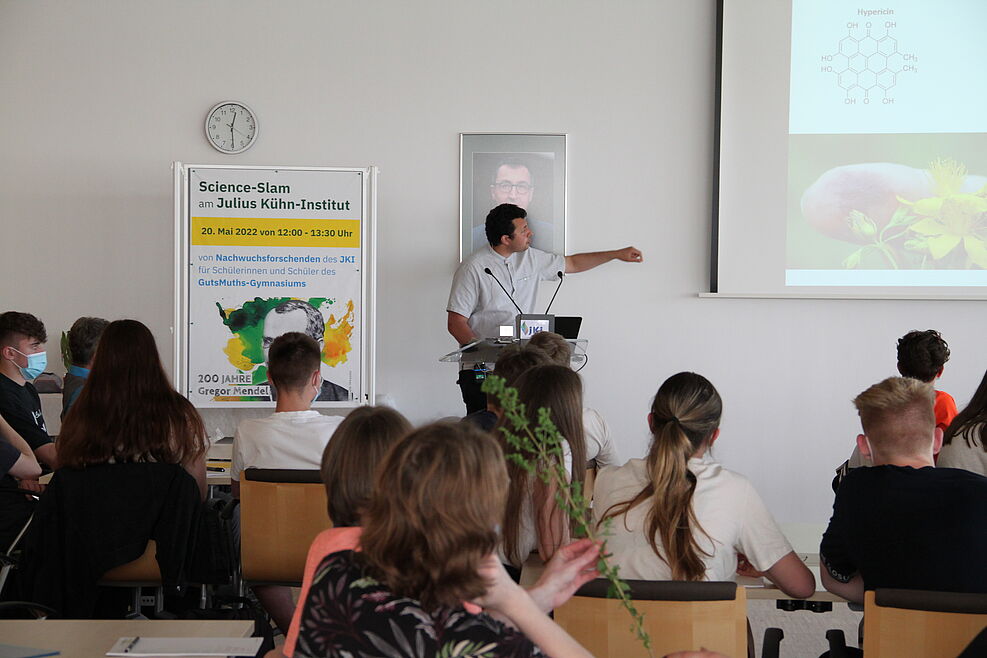 Ahmed El Menuawy deutet bei seinem Slam-Vortrag auf ein Bild der Strukturformel des Wirkstoffs Hypericin.